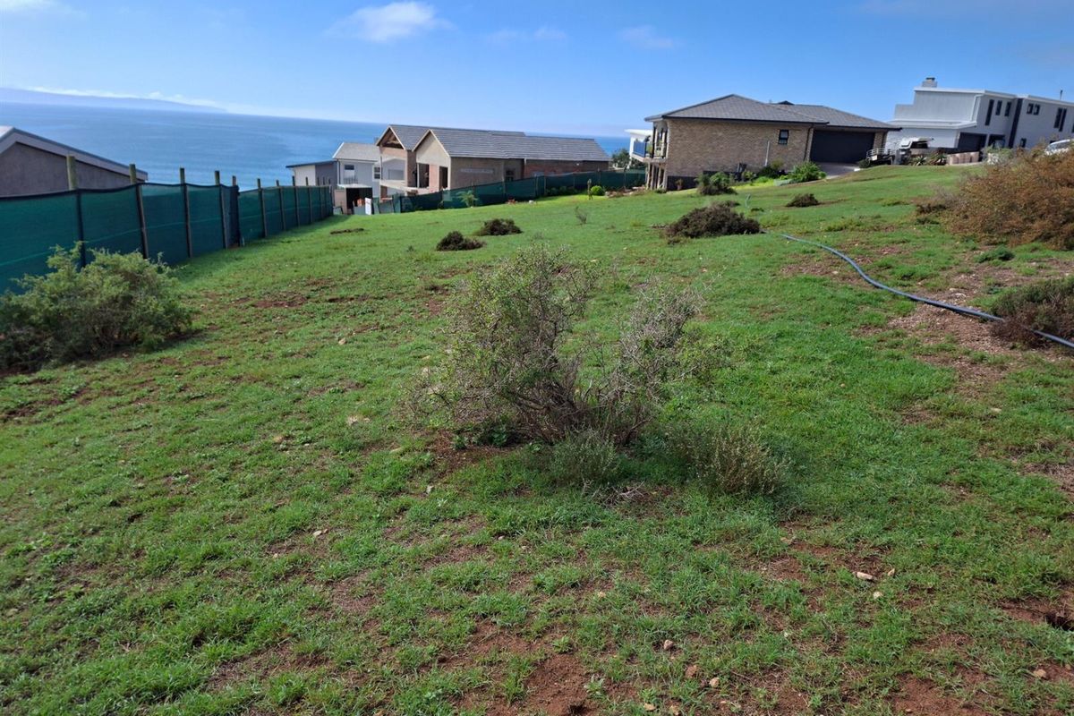 A sloping vacant residential plot featuring natural grass cover, perimeter fencing, and scenic ocean views in a developed coastal neighborhood.