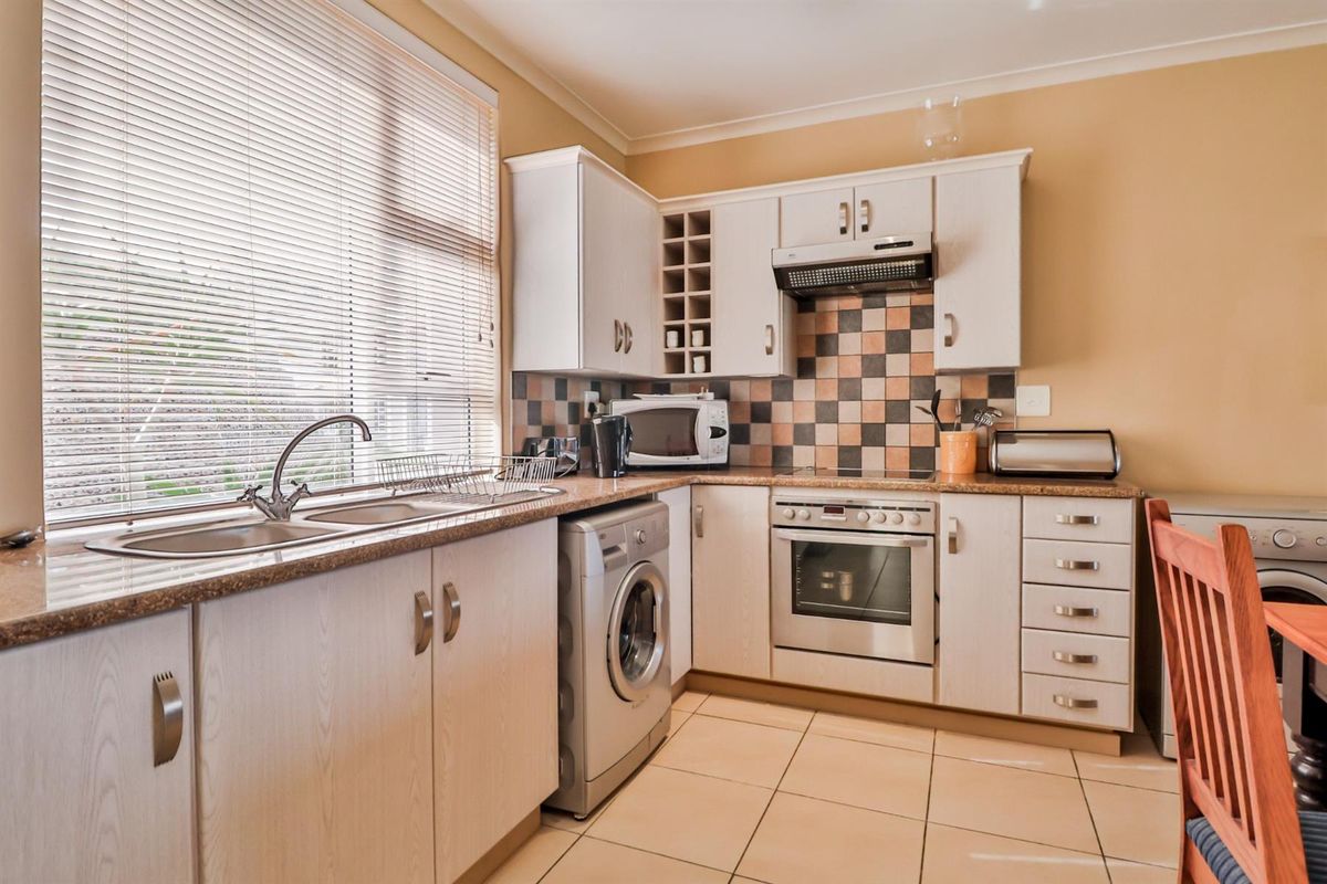 A functional kitchen featuring light-toned cabinetry, granite-look countertops, a built-in oven with extractor fan, and tiled flooring.