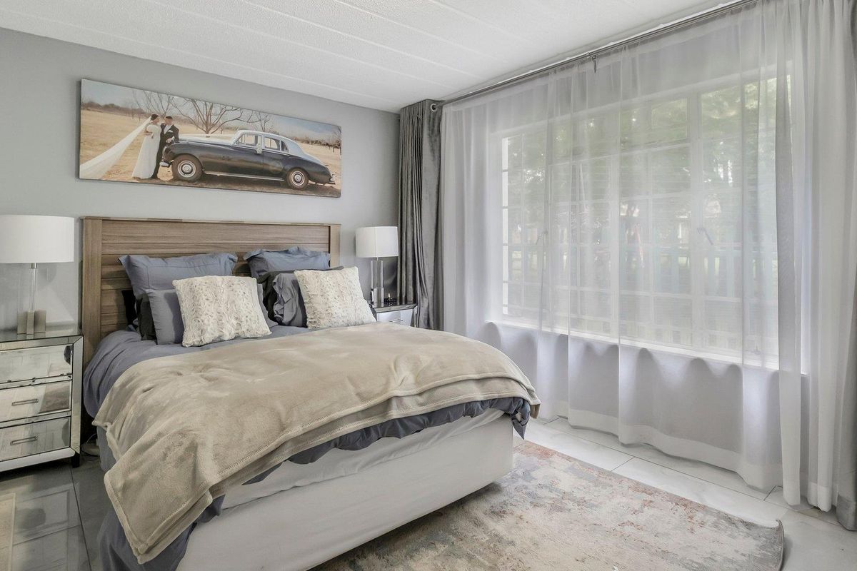 A well-maintained bedroom featuring large windows with sheer curtains, neutral wall tones, and tiled flooring.