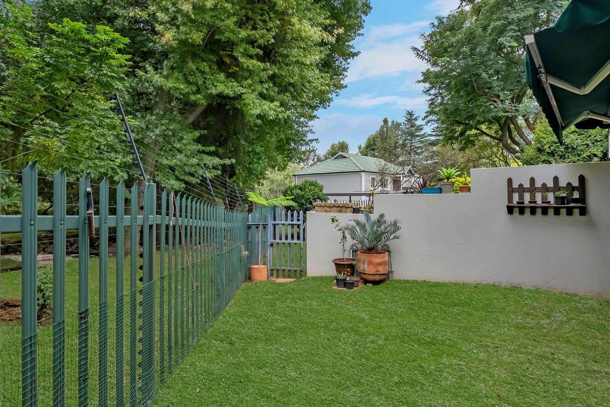 A private rear garden featuring a well-maintained lawn, secure perimeter fencing with electric wire, and a retractable patio awning.