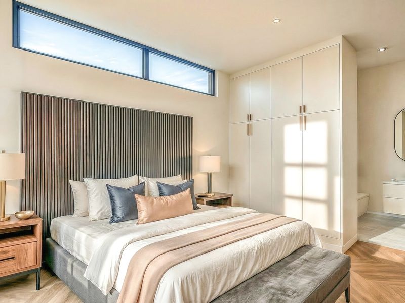 Modern bedroom featuring a slatted feature wall, clerestory window, built-in cabinetry, and an open-plan en-suite vanity area with herringbone flooring.