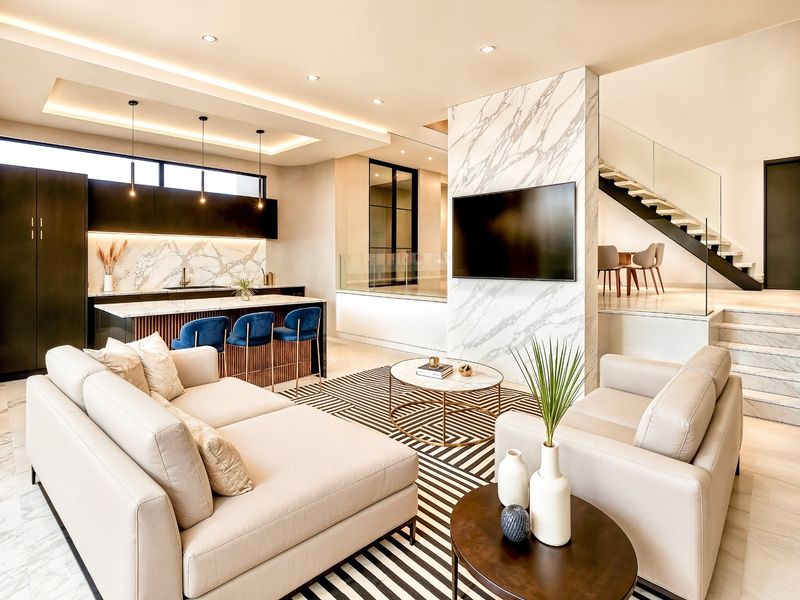 A modern open-plan living and kitchen area featuring marble finishes, a sleek kitchen island, and a striking staircase with a glass balustrade.