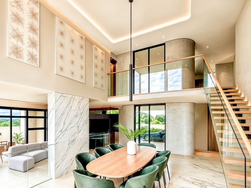 Spacious open-plan living and dining area featuring high ceilings, marble flooring, a striking floating staircase with glass balustrade, and a mezzanine level.