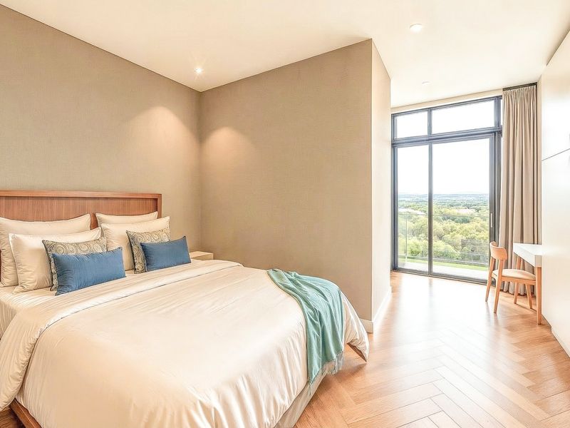Modern bedroom featuring herringbone timber flooring, built-in cabinetry, and floor-to-ceiling glass doors opening to a scenic balcony view.