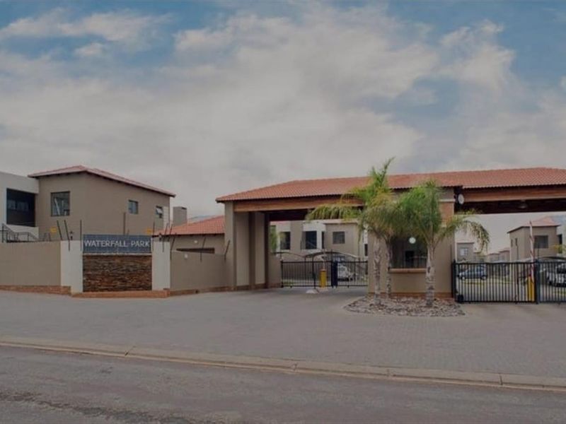 The main entrance to Waterfall Park townhouse complex, featuring a secure gated access point, perimeter walling, and paved driveway.