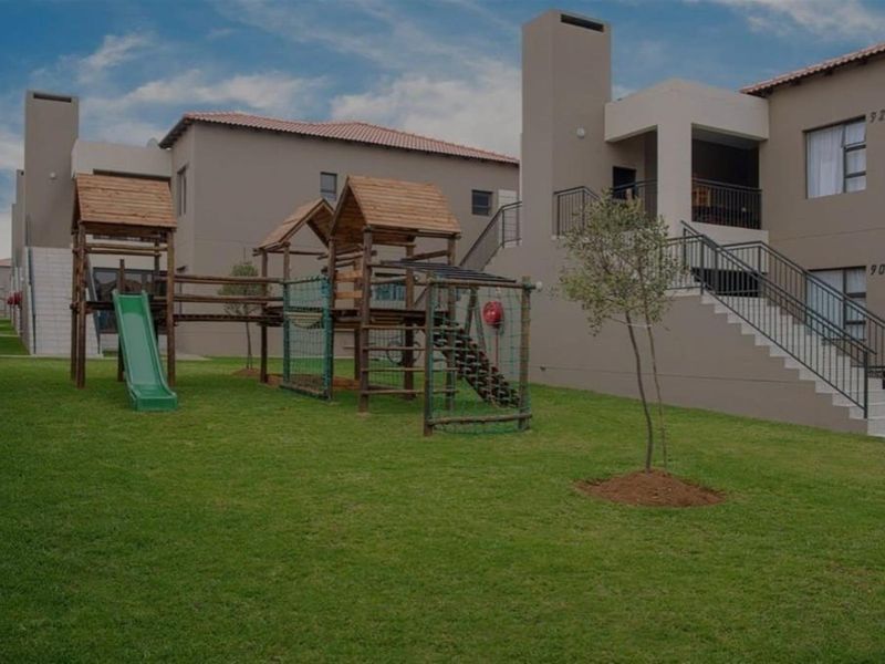 A well-maintained communal garden area featuring a children's playground, lawn, and access to the townhouse units with balconies and external staircases.