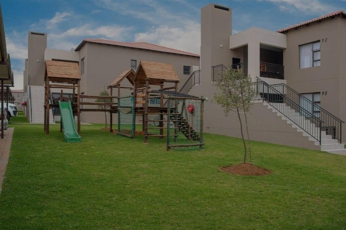 A well-maintained communal garden area featuring a children's playground, lawn, and access to the townhouse units with balconies and external staircases.