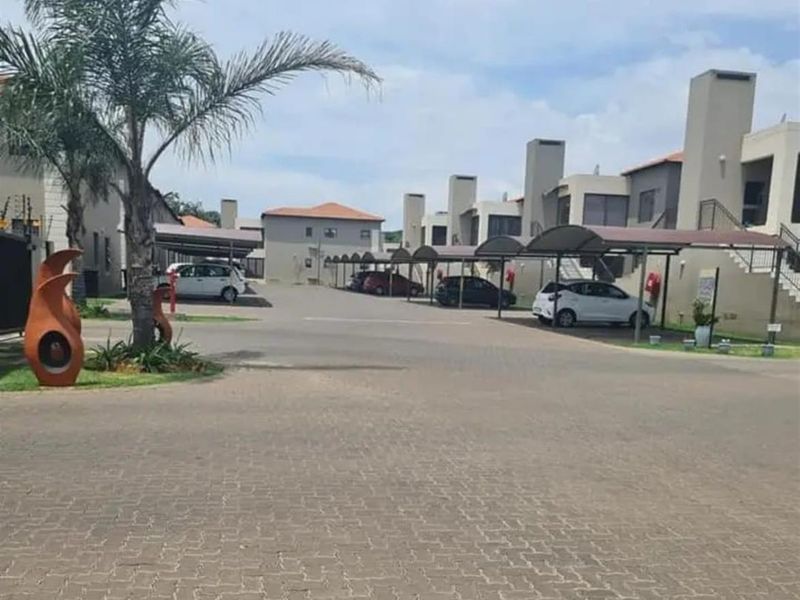 View of the townhouse complex driveway featuring paved surfaces, covered parking bays, and established residential units with chimney stacks.