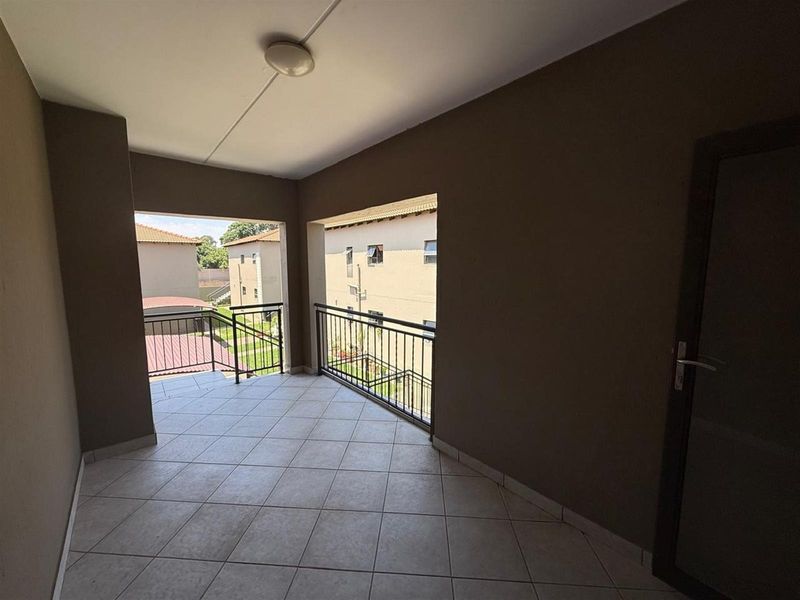 A covered balcony featuring tiled flooring and metal balustrades, offering an open view of the surrounding townhouse complex.