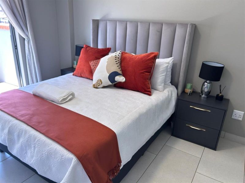 A well-maintained bedroom featuring neutral tiled flooring, a sliding door providing natural light, and modern wall finishes.