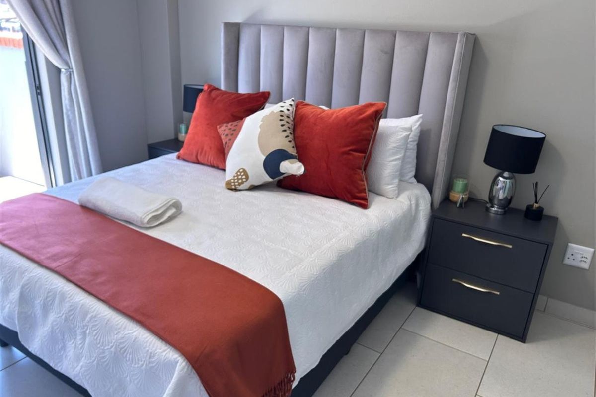 A well-maintained bedroom featuring neutral tiled flooring, a sliding door providing natural light, and modern wall finishes.