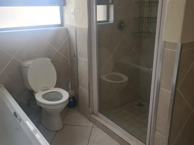 A functional bathroom featuring a bathtub, a separate shower enclosure with glass door, and neutral wall and floor tiling.