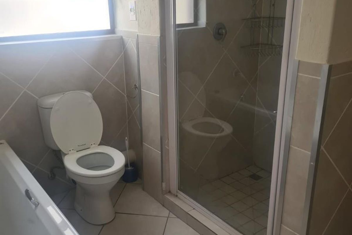A functional bathroom featuring a bathtub, a separate shower enclosure with glass door, and neutral wall and floor tiling.