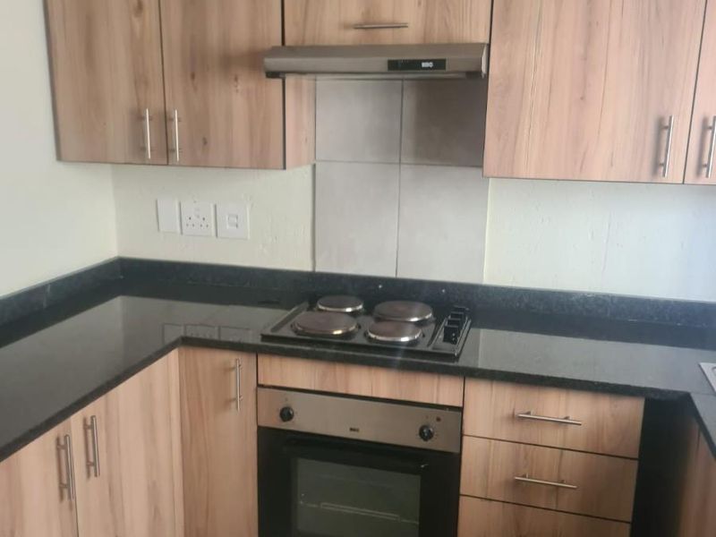 A functional kitchen featuring wood-look laminate cabinetry, dark granite countertops, a built-in oven, electric hob, and extractor fan with tiled flooring.