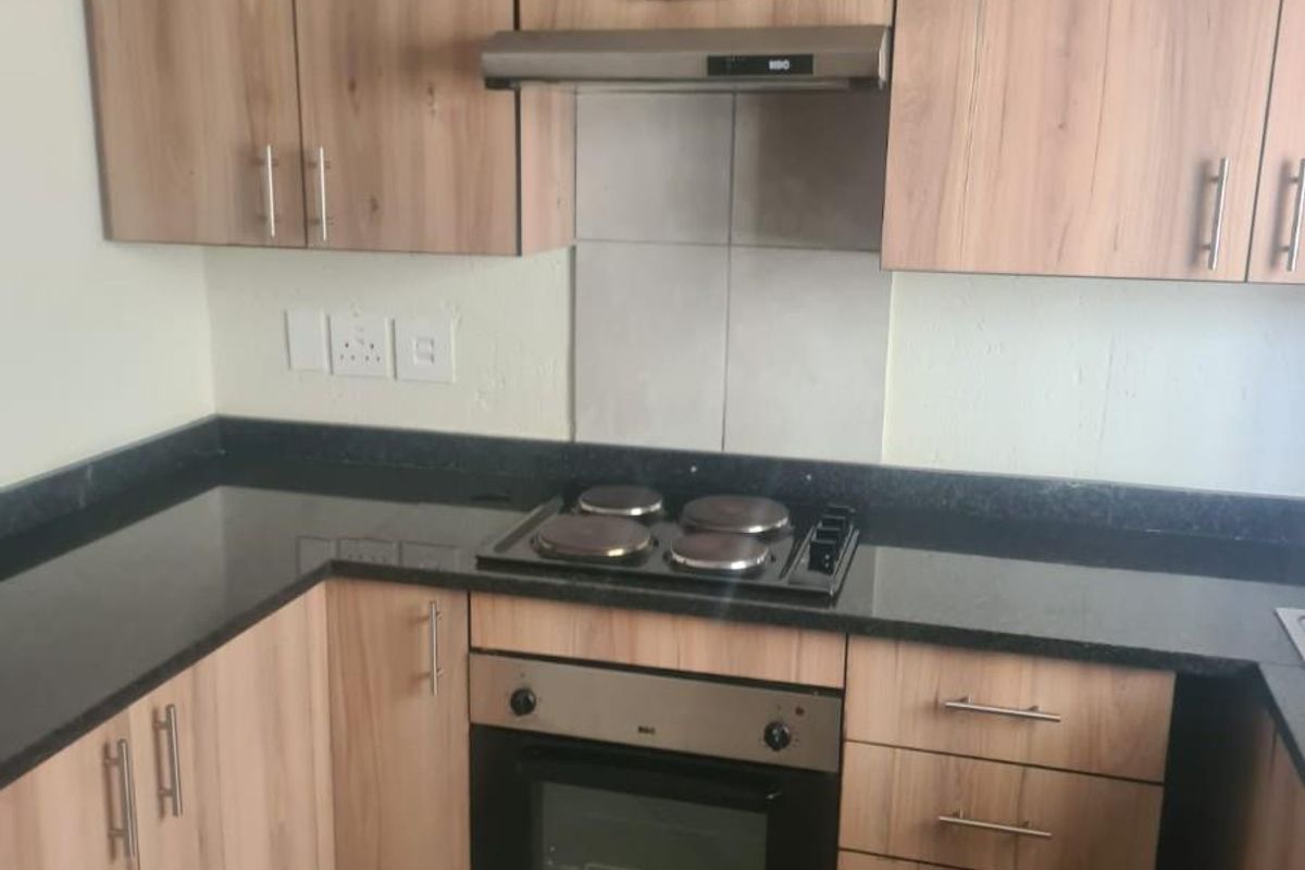 A functional kitchen featuring wood-look laminate cabinetry, dark granite countertops, a built-in oven, electric hob, and extractor fan with tiled flooring.