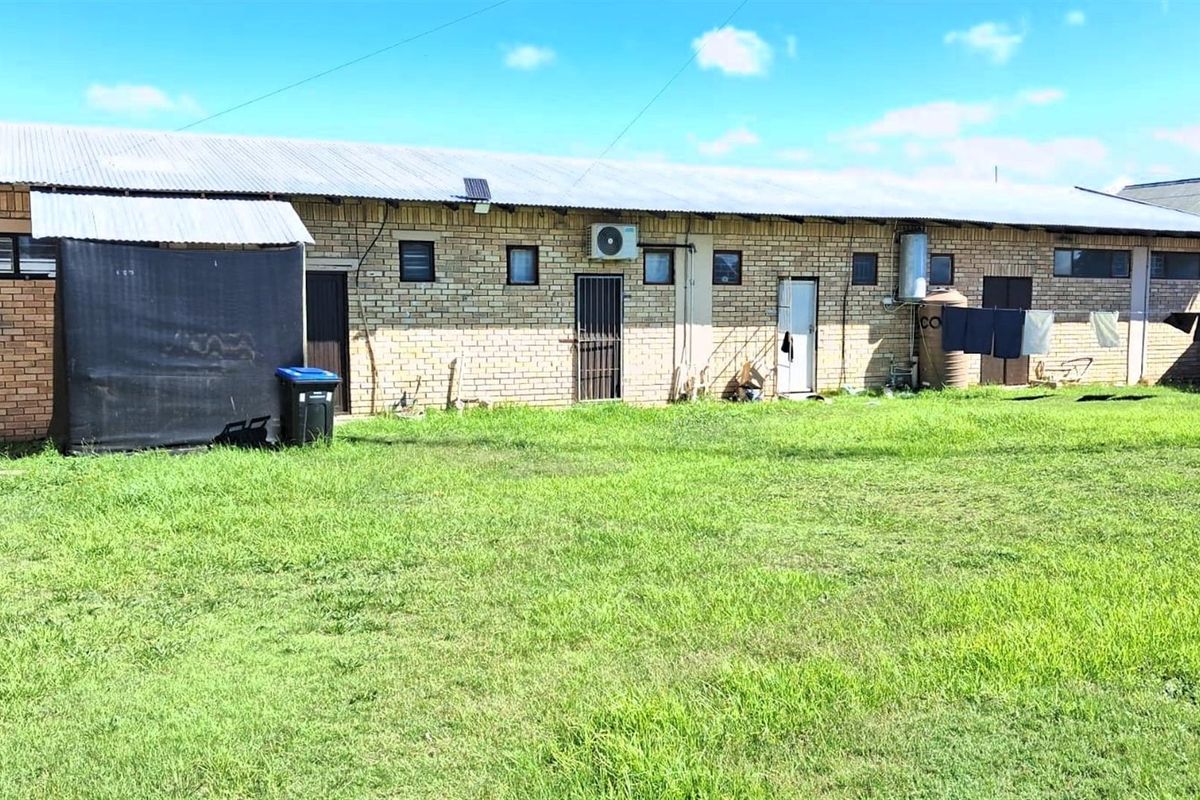 Rear view of a commercial building featuring face-brick exterior walls, corrugated metal roofing, and multiple access points opening onto a large grassed yard area.