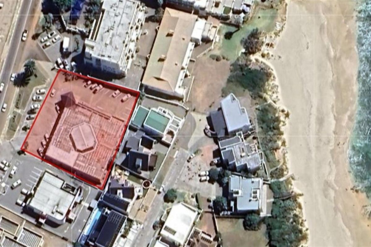 Aerial view of the commercial property highlighted in red, situated in a coastal location near the beach and surrounding infrastructure.