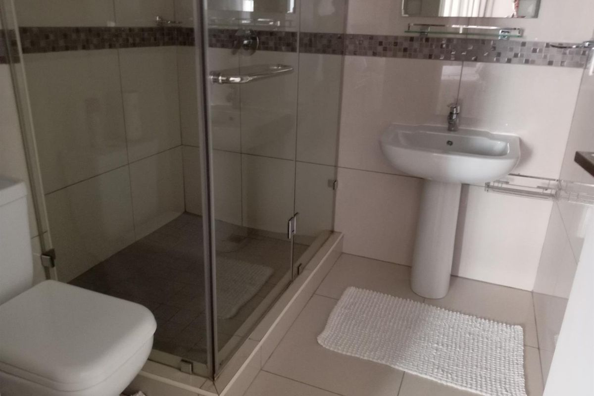 A functional bathroom featuring a glass-enclosed shower, a pedestal basin, and a toilet, finished with neutral wall and floor tiling.
