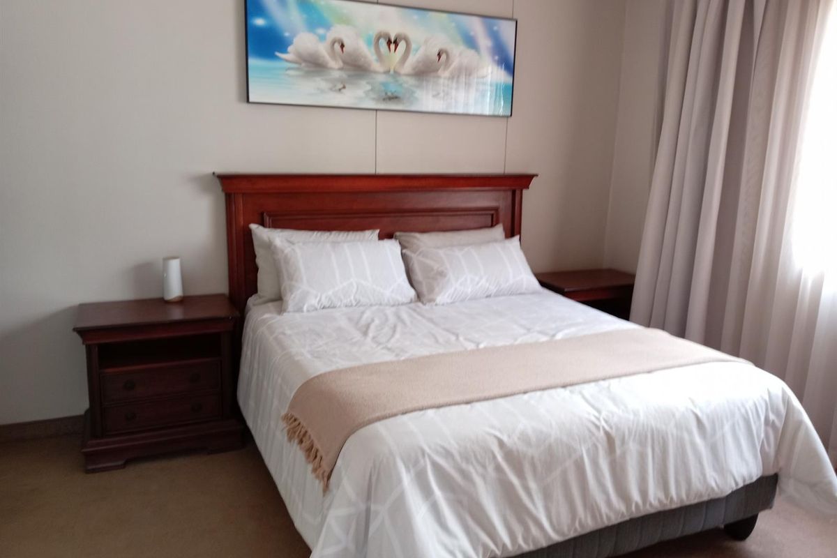 A well-maintained bedroom featuring neutral wall finishes, carpeted flooring, and full-length curtains.