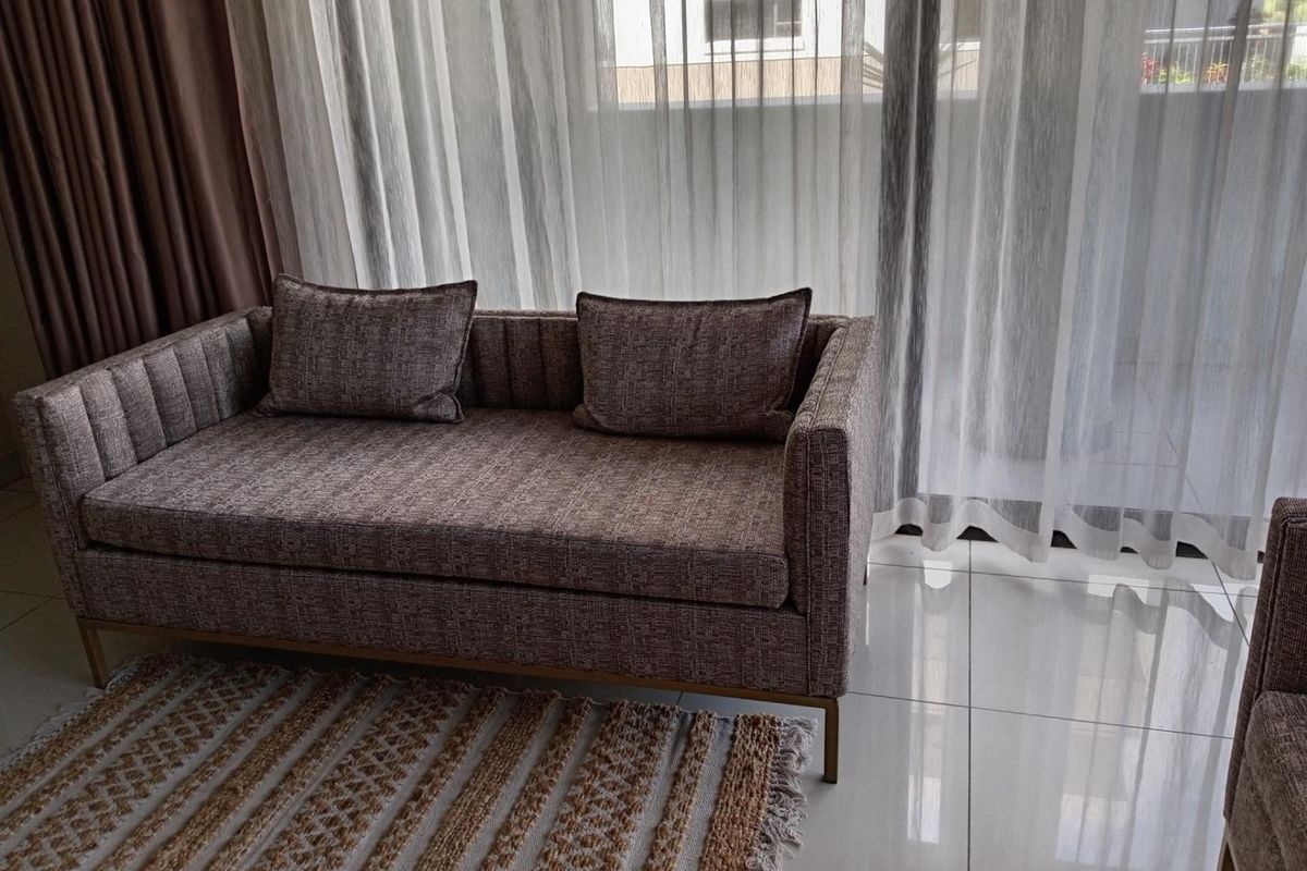 A bright living room area featuring large glass sliding doors with sheer curtains, leading to an outdoor space, finished with polished floor tiles.