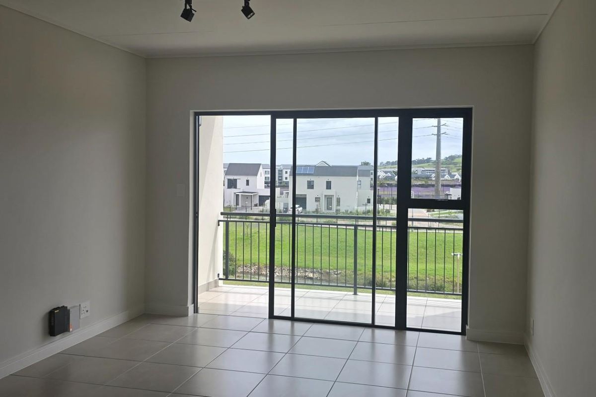 An empty, well-lit living area featuring neutral tiled flooring and a large sliding glass door that opens onto a private balcony.