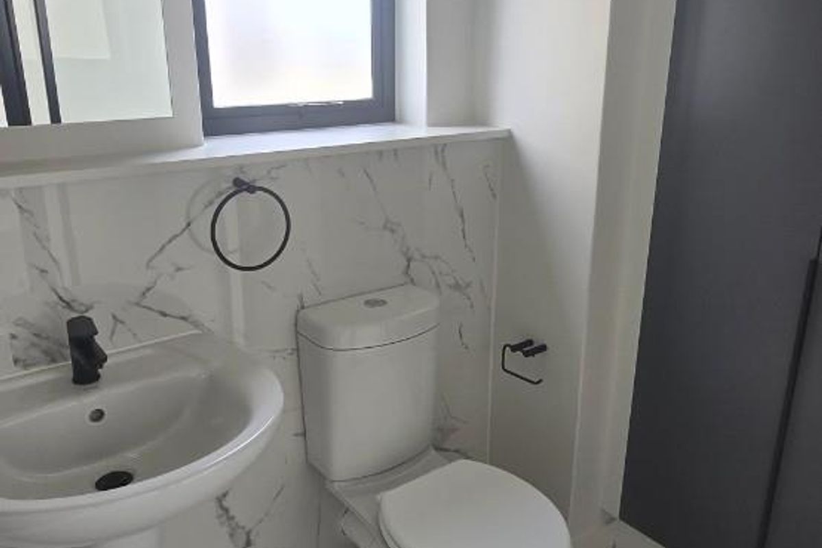 A modern, clean bathroom featuring a pedestal washbasin, toilet, marble-effect wall tiling, and neutral floor tiles with ample built-in storage.