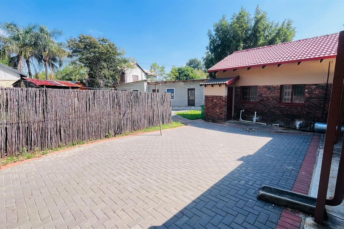 A paved rear courtyard area featuring brick exterior walls, a rustic reed fence, and direct access to the main dwelling.
