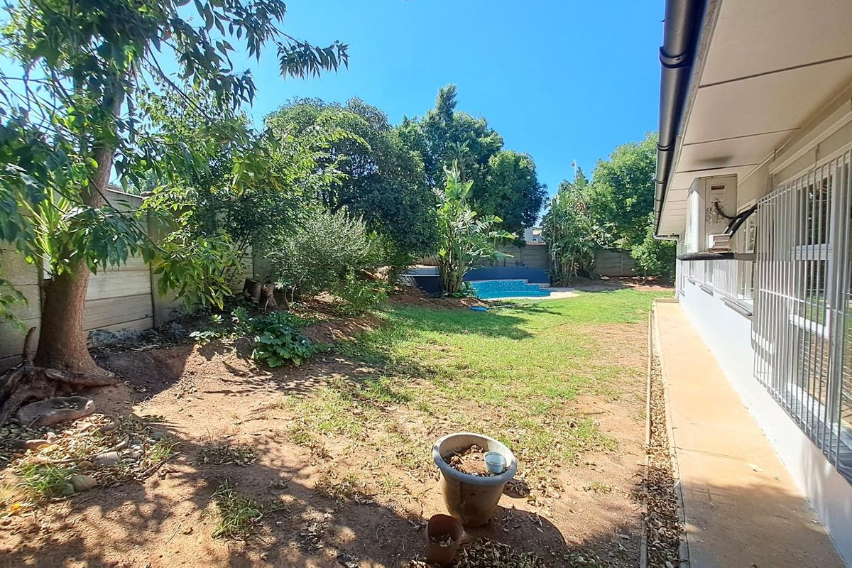 A spacious rear garden featuring a swimming pool, established trees, and a paved walkway along the side of the house.