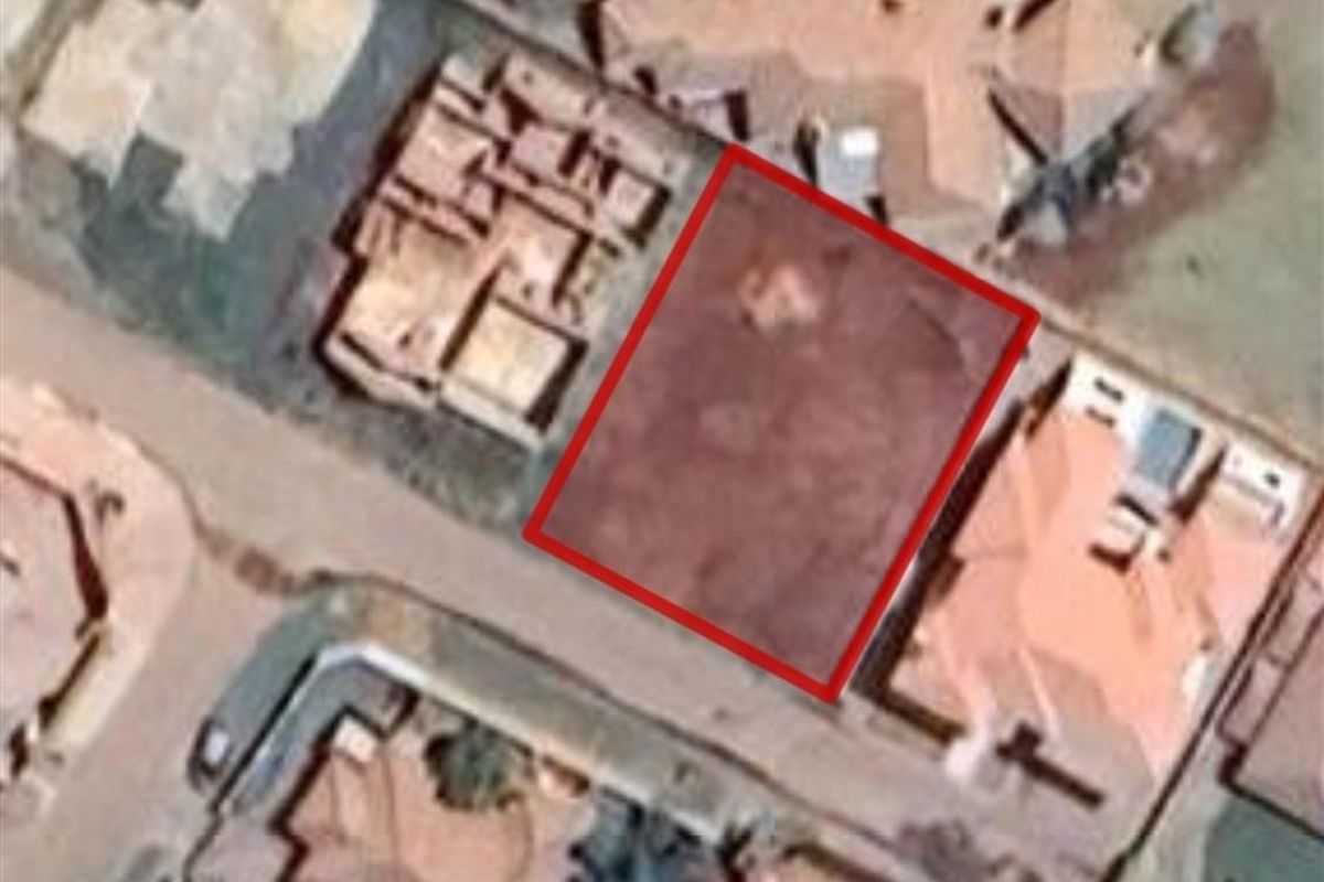 Aerial view of a vacant residential plot highlighted in red, situated within an established suburban neighborhood.
