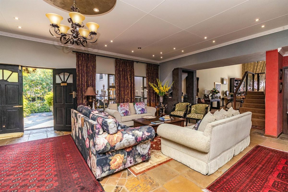Spacious living room featuring stone flooring, recessed ceiling lighting, a decorative chandelier, and an open staircase leading to the upper level.