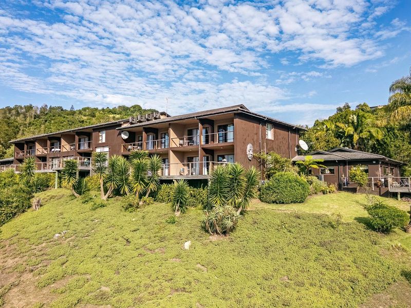 A multi-level residential building featuring private balconies, dark exterior finishes, and landscaped grounds set against a hillside backdrop.