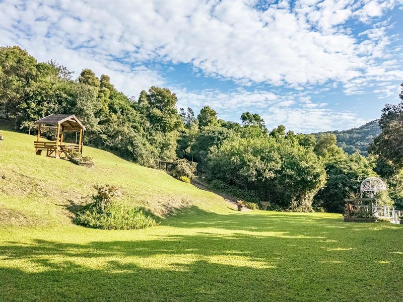 Expansive, well-maintained sloping garden area featuring mature trees, lush green lawn, and a wooden gazebo structure.