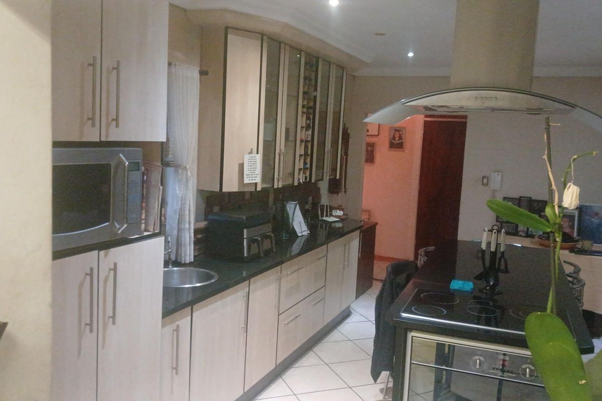 A functional kitchen featuring light-toned cabinetry, dark granite countertops, a central island with a built-in hob and oven, and tiled flooring.
