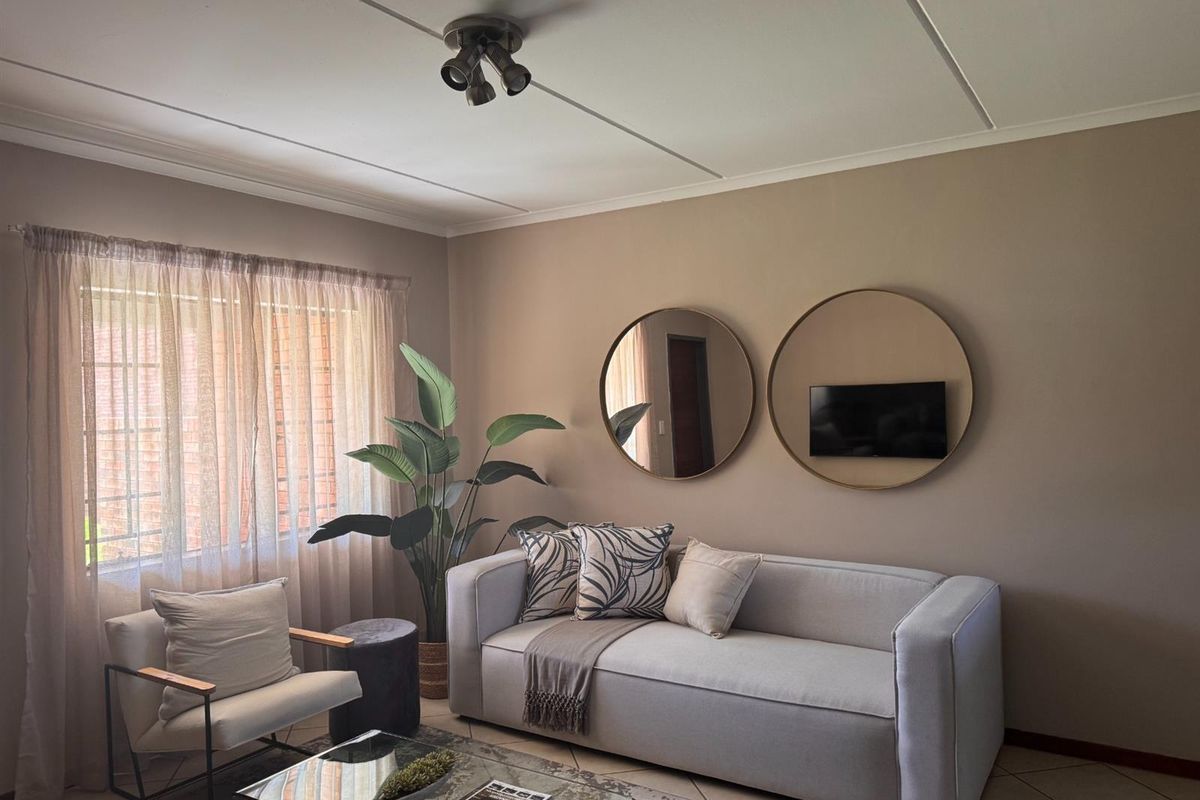 A well-maintained living room featuring neutral wall tones, tiled flooring, and a ceiling-mounted spotlight fixture, providing a comfortable and inviting atmosphere.