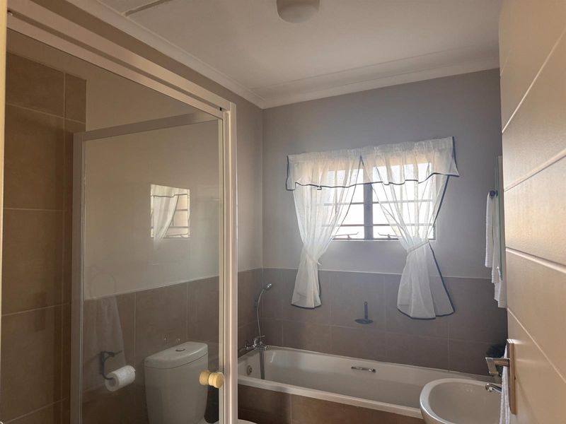 A functional bathroom featuring a built-in bathtub, separate glass-enclosed shower, pedestal basin, and neutral wall tiling.