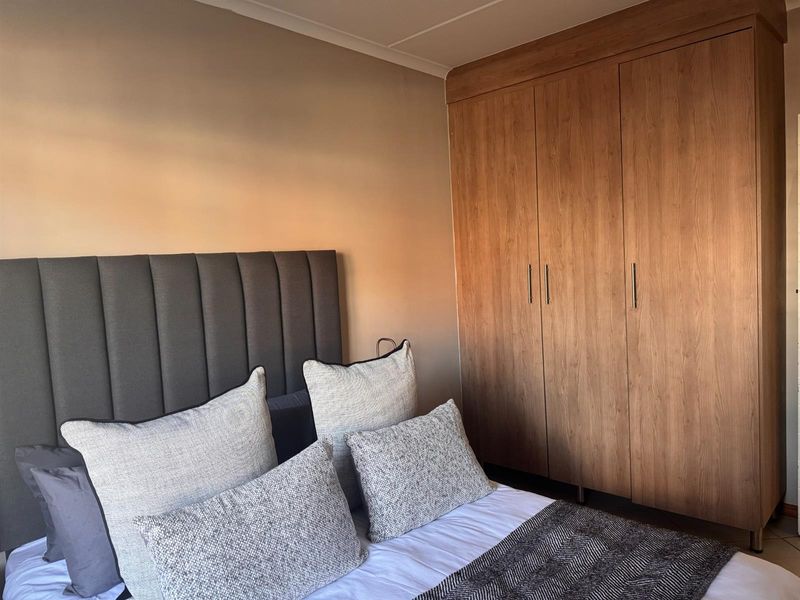 A well-maintained bedroom featuring a large, modern wood-finish built-in wardrobe providing ample storage space.