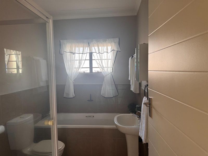 A functional bathroom featuring a pedestal basin, built-in bathtub, and a separate glass-enclosed shower with neutral wall tiling.