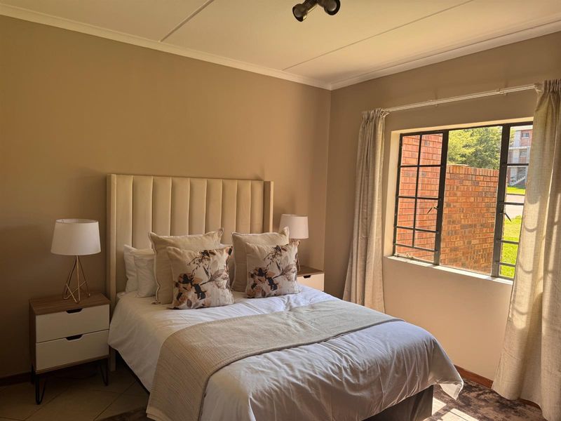A well-lit bedroom featuring neutral wall tones, tiled flooring, and a large steel-framed window allowing for natural light.