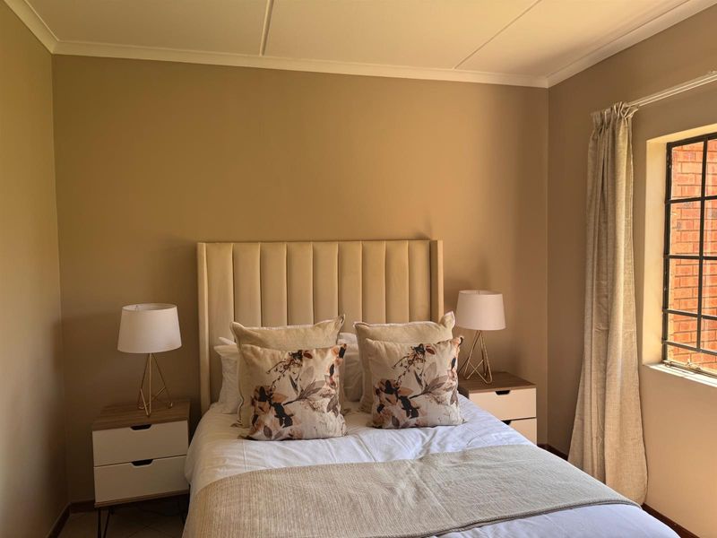 A well-maintained bedroom featuring neutral wall tones, a coved ceiling, and a window fitted with security bars.