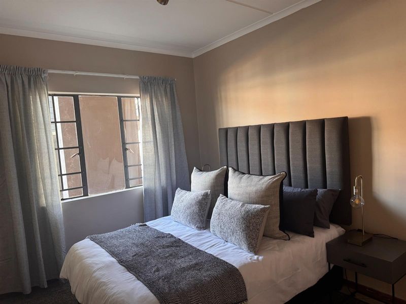 A cozy bedroom featuring neutral wall tones, a metal-framed window, and decorative cove cornicing, providing a comfortable and well-lit sleeping space.
