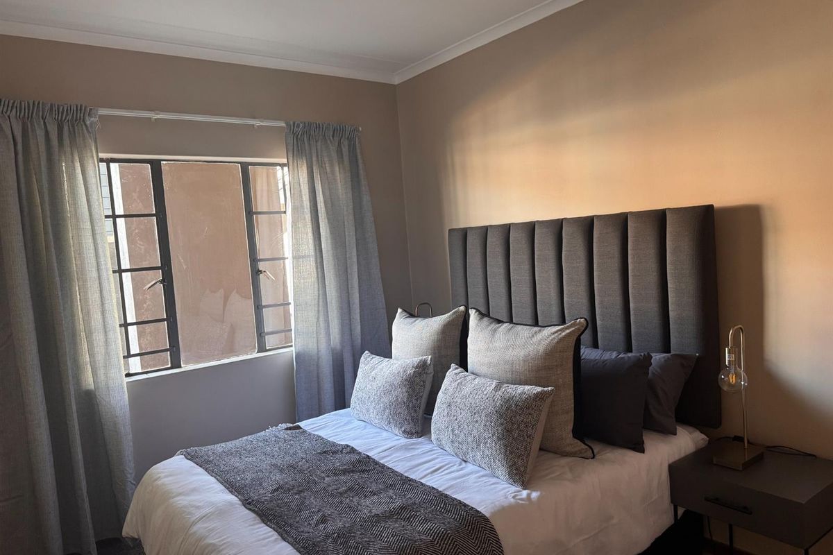 A cozy bedroom featuring neutral wall tones, a metal-framed window, and decorative cove cornicing, providing a comfortable and well-lit sleeping space.