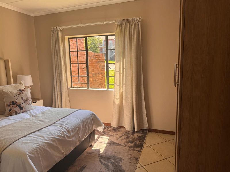 A bedroom featuring tiled flooring, a built-in wardrobe, and a steel-framed window allowing natural light into the space.