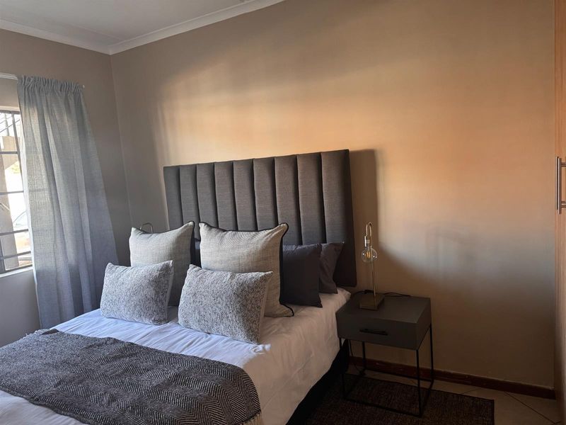 A cozy bedroom featuring neutral wall tones, a window with curtains, and a built-in cupboard for storage.