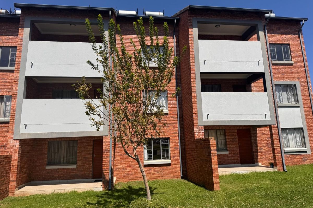A view of the rear elevation of a multi-story apartment complex featuring face brick construction, private balconies, and ground-floor patio areas.