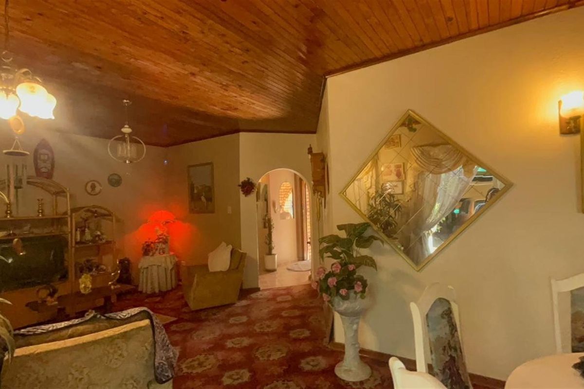A living area featuring a distinctive timber-clad vaulted ceiling, an arched entryway, and wall-mounted lighting, offering a dated aesthetic ready for modernization.