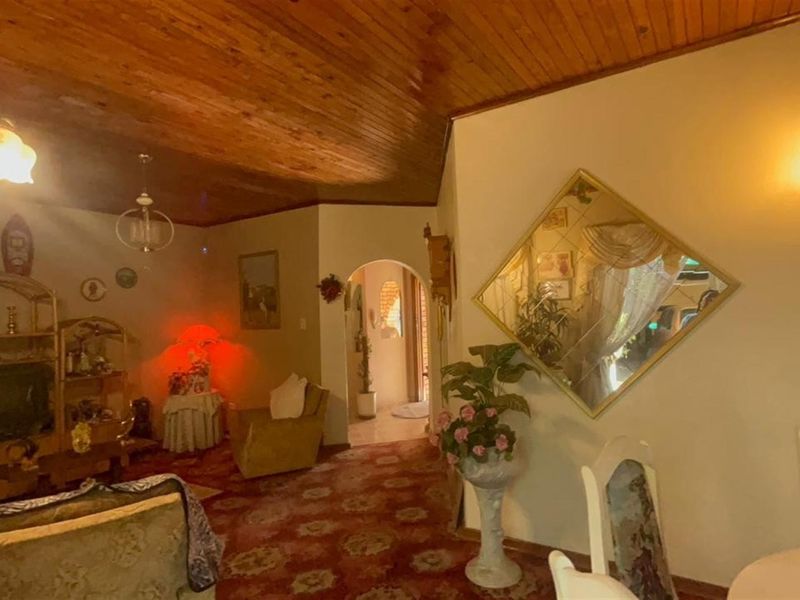 A living area featuring a distinctive timber-clad vaulted ceiling, an arched entryway, and wall-mounted lighting, offering a dated aesthetic ready for modernization.