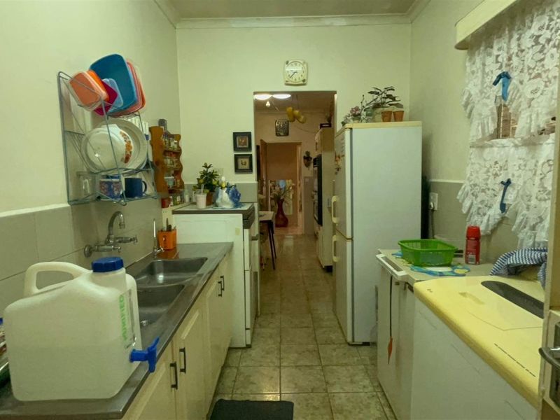 A functional galley-style kitchen featuring tiled flooring, a double stainless steel sink, and built-in cabinetry with a tiled splashback.