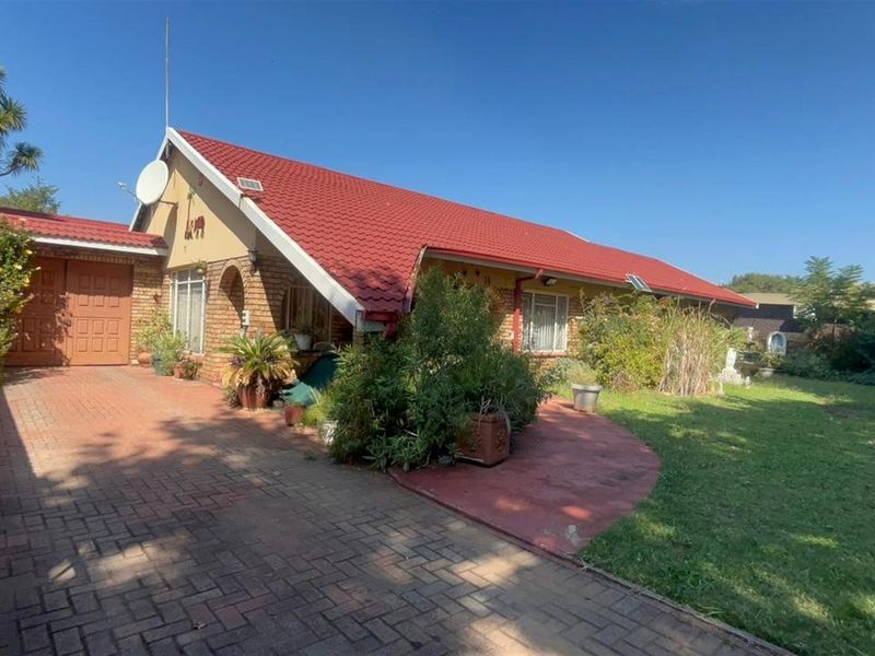 Front view of a single-story brick house featuring a prominent red tiled roof, paved driveway, and established garden area.