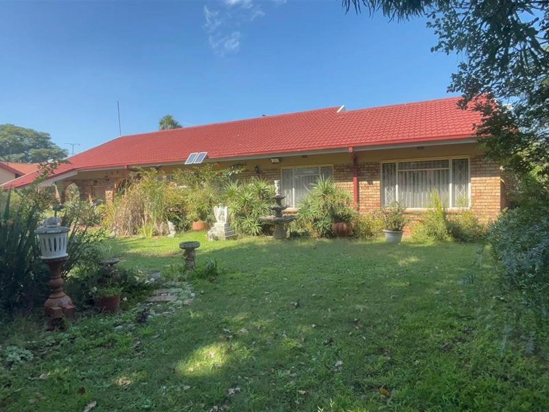 A rear view of a single-story brick house featuring a red tiled roof, security bars on windows, and a spacious garden area.