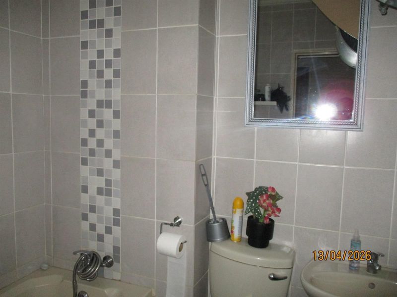A functional bathroom featuring tiled walls with a mosaic accent, a built-in bathtub, a toilet, and a wall-mounted mirror.